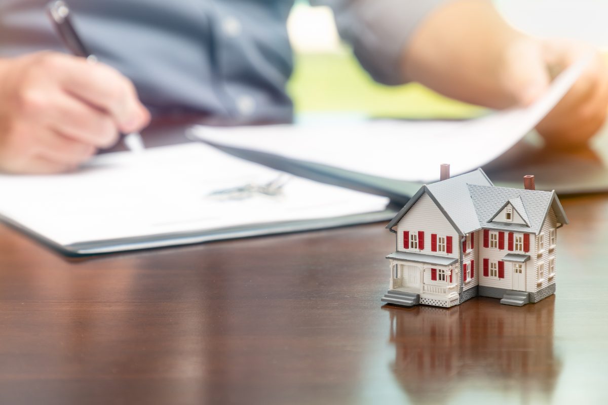 firma de un contrato de hipoteca con maqueta de casa, seguro de vida hipotecario obligatorio